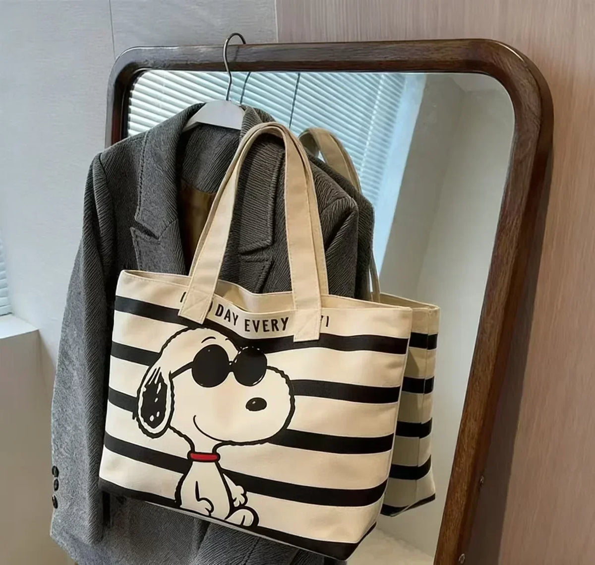 A beige and black striped canvas shoulder bag featuring a Snoopy cartoon face design, displayed on a hanger.