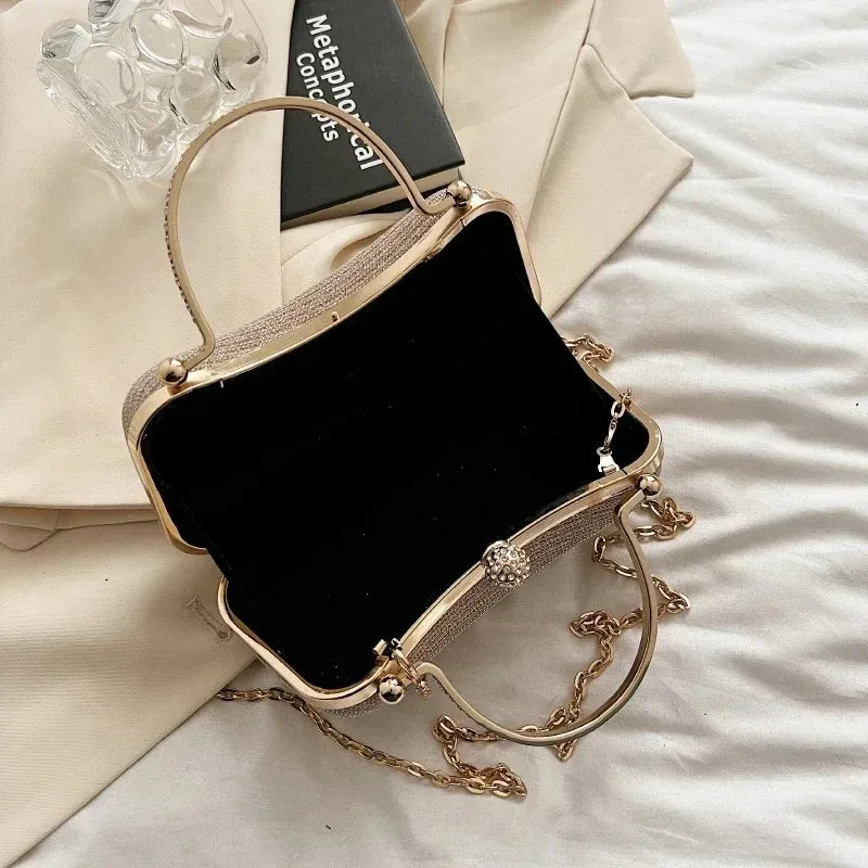 A gold glitter crossbody evening clutch bag resting on a light fabric background.