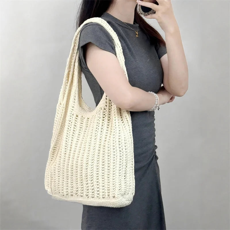 A woman holds a cream-colored bohemian knit shoulder bag against a gray background.