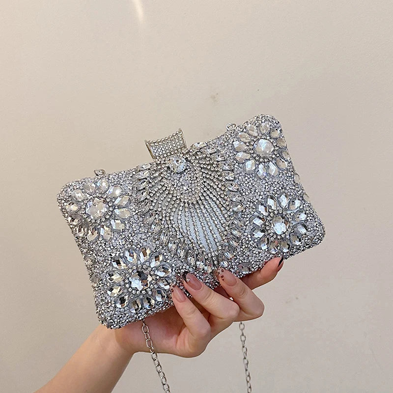A hand holds a silver rhinestone evening clutch bag decorated with sparkling stones.