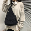 A person wearing a beige sweatshirt holds a black canvas crossbody shoulder bag with multiple pockets.