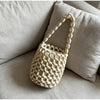 A cream-colored beaded clutch bag with a woven texture resting on a light gray sofa cushion.