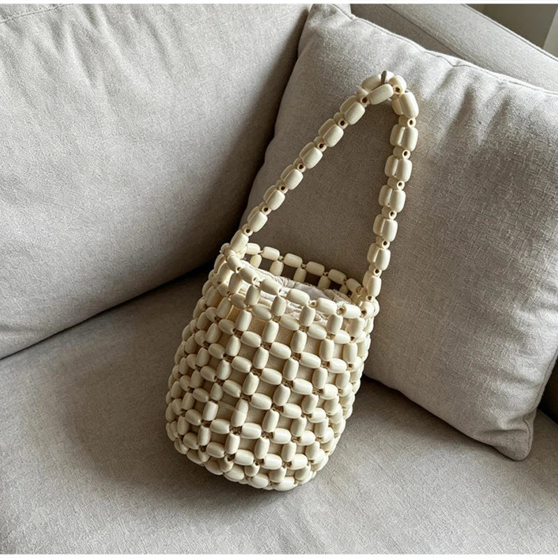 A cream-colored beaded clutch bag with a woven texture resting on a light gray sofa cushion.