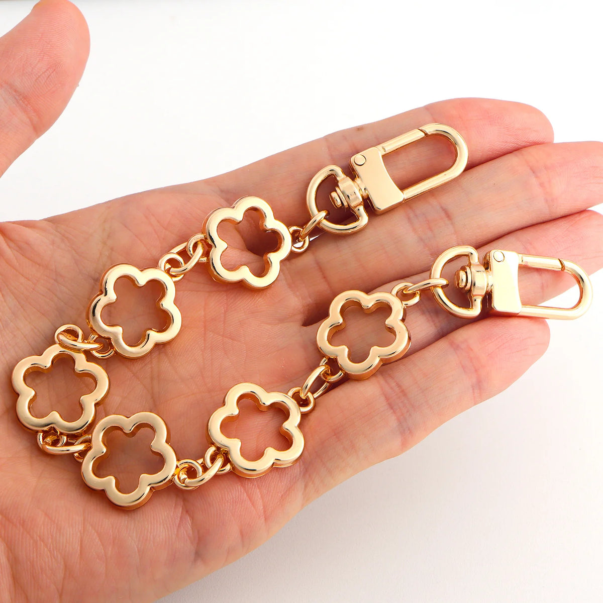 A gold-colored flower motif chain extender with a clasp is shown being held in a hand.