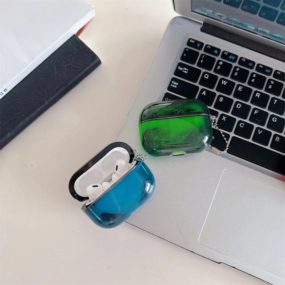 A green luminous sand effect earphone case and a blue AirPods charging case are placed on a silver laptop.