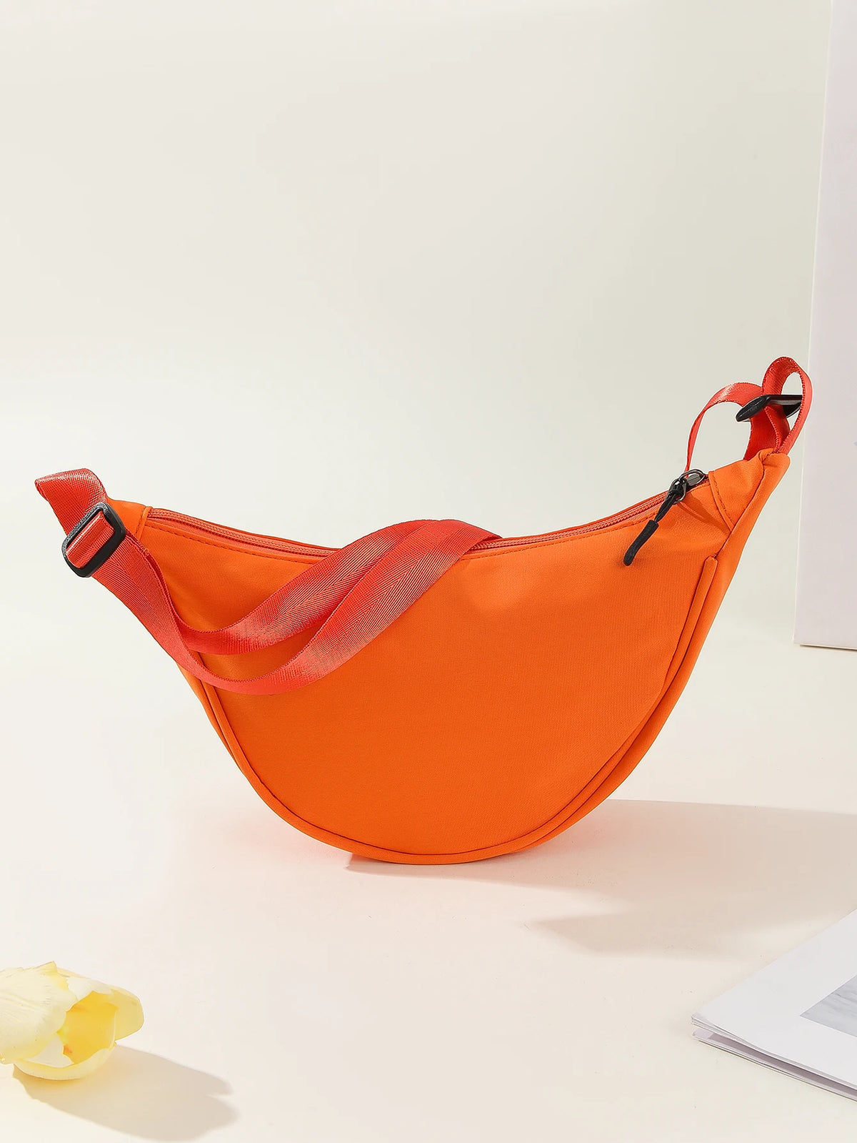 An orange women's preppy sling crossbody bag with a red strap is displayed on a light surface.