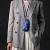 A gray blazer worn over a white top, featuring a blue leather lanyard and storage case hanging from it.