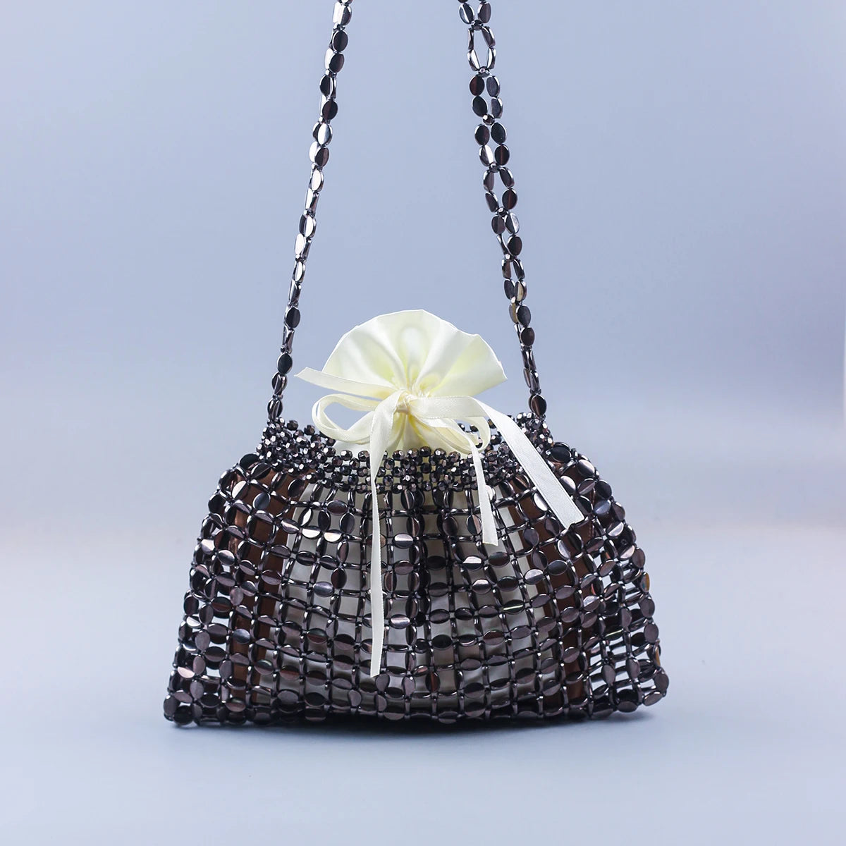A handmade dumpling bag covered in dark silver and gold beads with a cream ribbon bow.