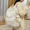 Una persona con suéter color crema lleva una mochila de múltiples bolsillos con estampado floral azul claro y un osito de pel