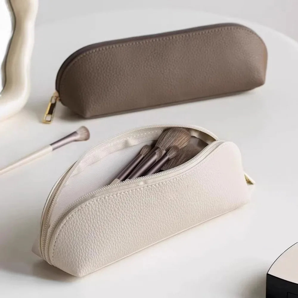 A beige makeup pouch with a zipper is shown next to a larger gray pouch containing makeup brushes.