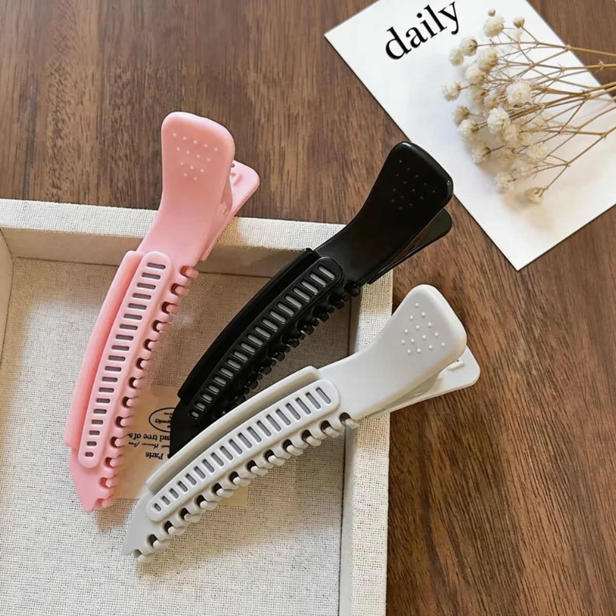 Collection de pinces à cheveux professionnelles roses et blanches antidérapantes pour le styling, présentées dans une boîte.