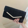 A black glitter pleated crossbody clutch bag with a light colored trim is held by a hand.