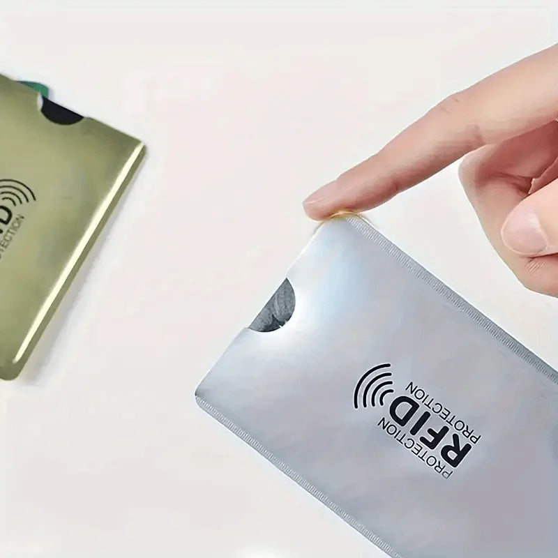 A hand is placing a silver RFID protection card sleeve onto a green card.