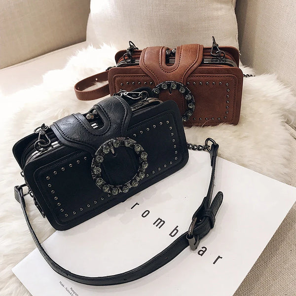 A black vintage PU leather crossbody bag with a rhinestone buckle resting on a white card.