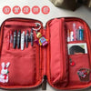 A red corduroy pencil case with a fold-out tray is shown open, displaying various stationery items inside.
