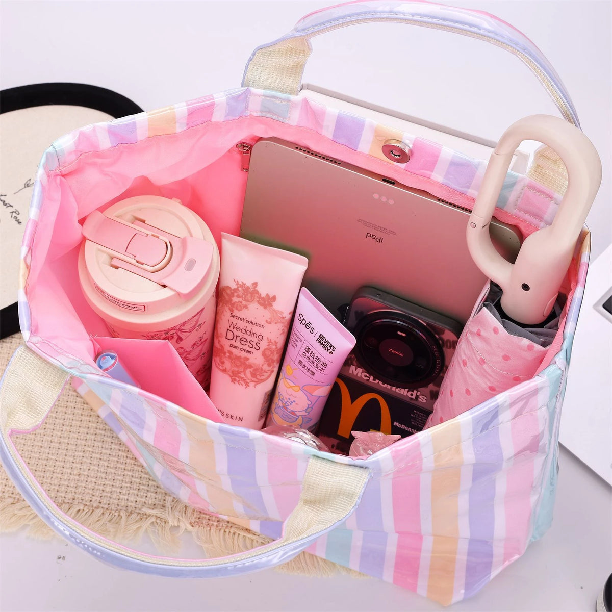 A pink and white striped waterproof PVC shoulder tote bag filled with various cosmetic products.