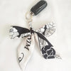 Lazo de cinta de seda floral blanco y negro con lazo, unido a un anillo de llavero plateado.