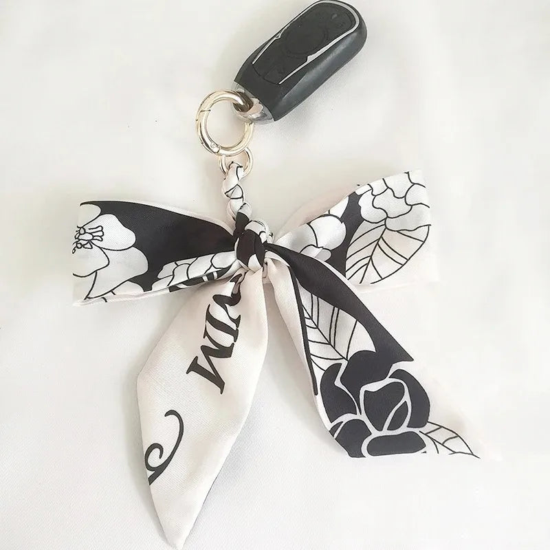 Lazo de cinta de seda floral blanco y negro con lazo, unido a un anillo de llavero plateado.