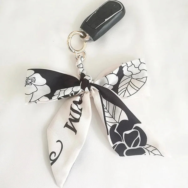 A white and black floral patterned silk ribbon bow attached to a silver keychain ring.