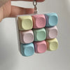 A hand holds a clear plastic container filled with colorful, square tactile stress relief keyboard fidget toys.