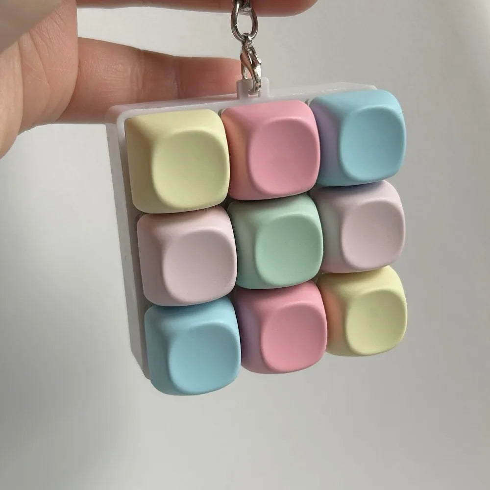 A hand holds a clear plastic container filled with colorful, square tactile stress relief keyboard fidget toys.