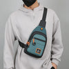 A person wearing a light gray hoodie is holding an olive green nylon chest bag with black straps.