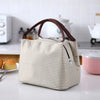 A beige and brown striped thermal lunch bag with a handle resting on a white countertop.