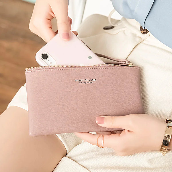 A pink minimalist PU leather zipper wallet holding a smartphone and cards, shown in a close-up on a person's hand.