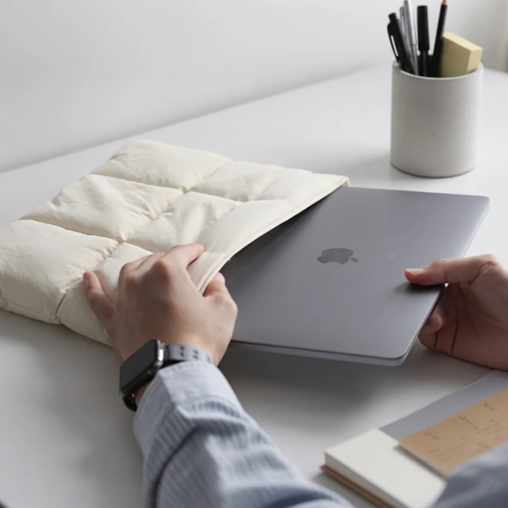 Une personne place un ordinateur portable dans une housse rembourrée et matelassée sur un bureau blanc.