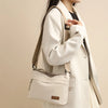 A woman holds a beige nylon crossbody shoulder bag with multiple zippered compartments against a light background.