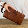 Une main tient un porte-monnaie/sac pochette en cuir marron sur une surface en bois.