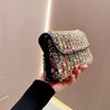 A hand holds an elegant rhinestone leather evening clutch bag with multicolored embellishments against a light background.