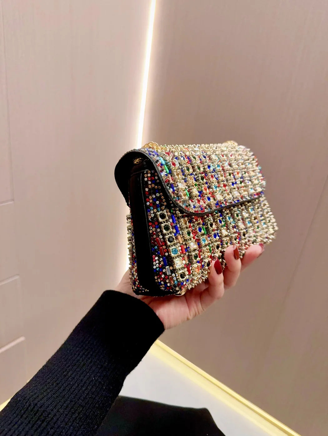 A hand holds a luxury rhinestone evening clutch bag with multicolored sparkling embellishments.