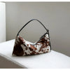 A brown and white cowhide crossbody bag with black leather strap resting on a white surface.