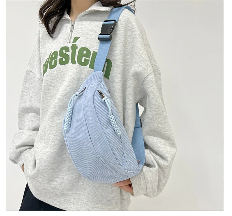 A light blue corduroy waist pack is worn by a woman in a gray hoodie.