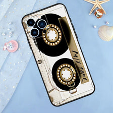 A phone case featuring a vintage cassette tape design with gold and black accents on a light blue background.