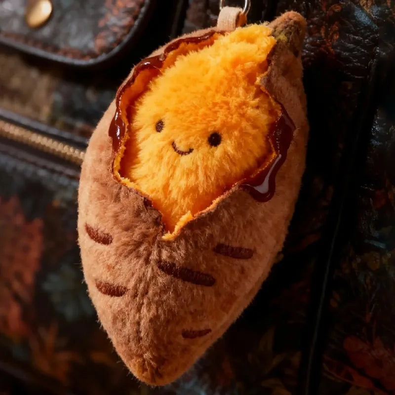 A fluffy orange sweet potato plush keychain with a carved face and a brown glaze, attached to a dark leather item.
