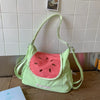 A lime green nylon messenger backpack shaped like a watermelon slice is displayed on a wooden surface.