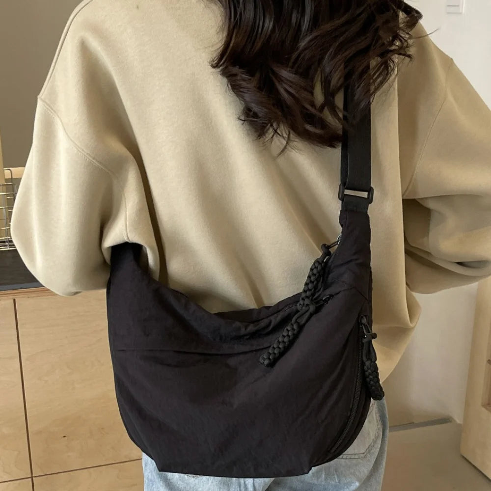 A black canvas crossbody shoulder bag worn by a person, shown from the back and side.