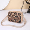 A beige leopard print crossbody bag with a tan strap is shown on a white surface.