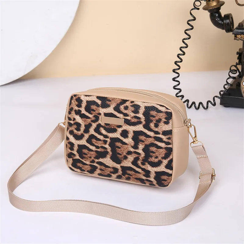 A beige leopard print crossbody bag with a tan strap is shown on a white surface.
