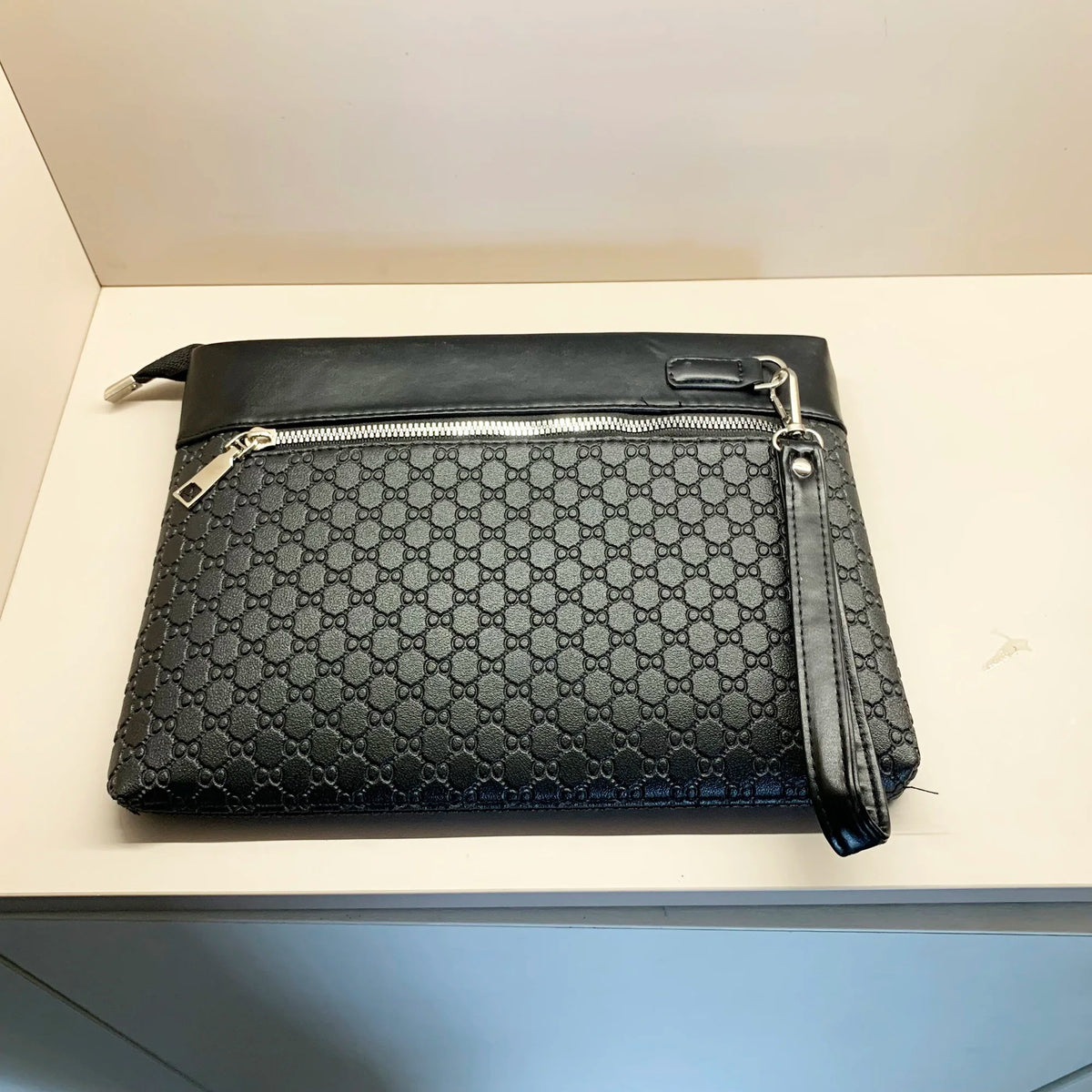 A black quilted PU leather clutch bag with a silver zipper and chain strap resting on a white surface.