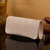 A rolled satin evening clutch in a pale pink color resting on a dark reflective surface.