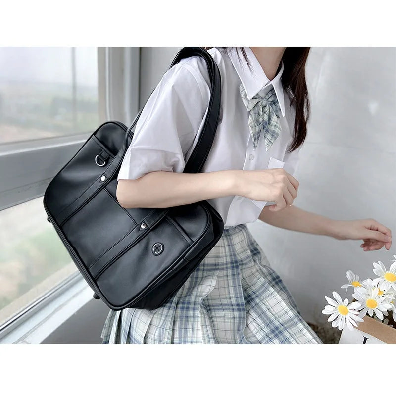 A woman wearing a white shirt and plaid skirt holds a black PU shoulder bag by a window.