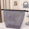 Un sac de rangement à cordon en filet gris est exposé sur une surface blanche à côté d'un support en verre et métal.