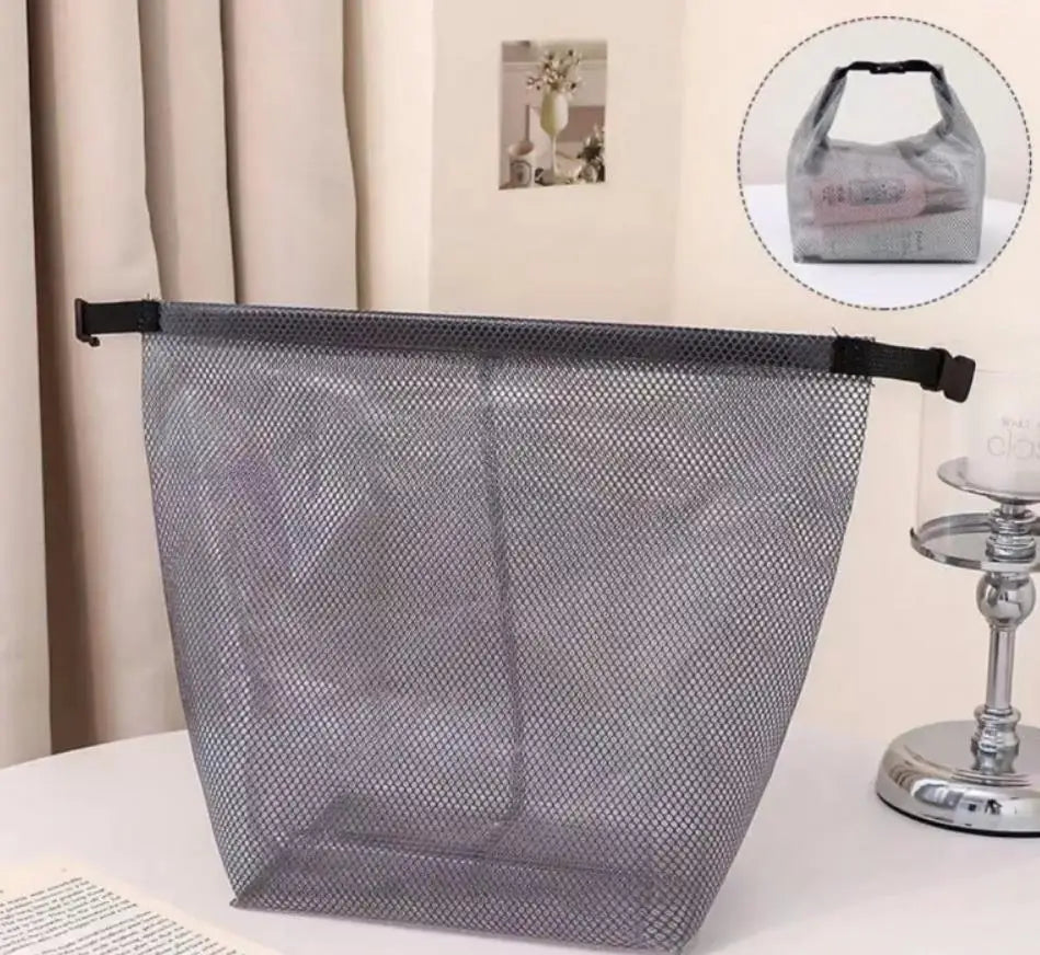 Un sac de rangement à cordon en filet gris est exposé sur une surface blanche à côté d'un support en verre et métal.