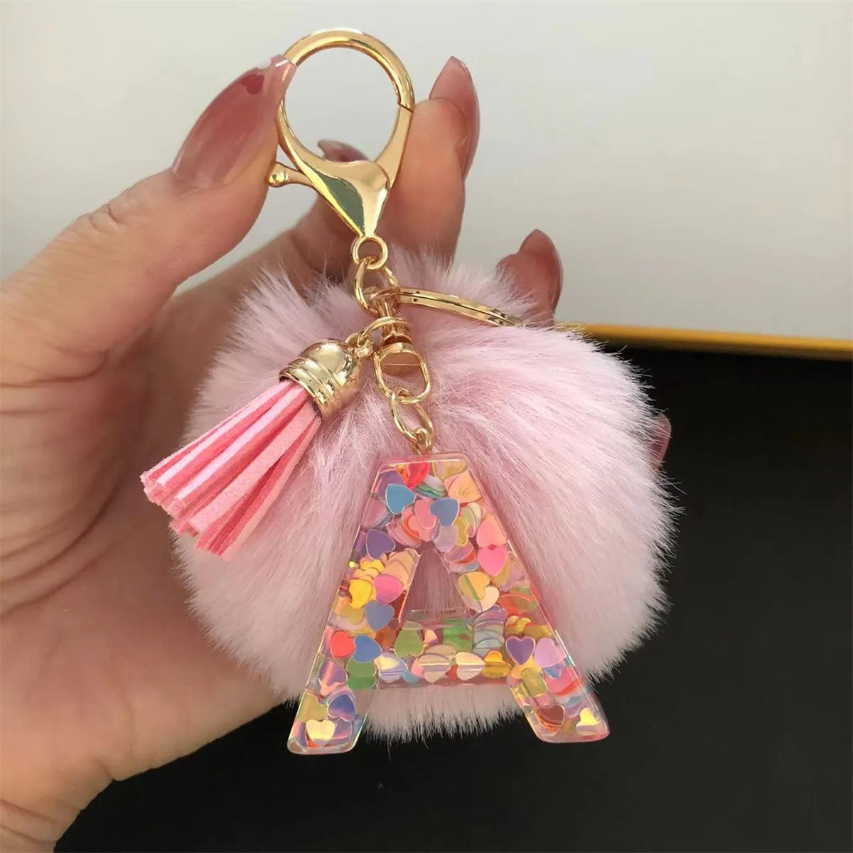 A custom initial letter keychain featuring a shiny resin pendant with a pink alphabet charm and tassels.