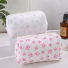 Bolsas de maquillaje acolchadas blancas con estampados de lazo rosa, exhibidas sobre una superficie blanca.