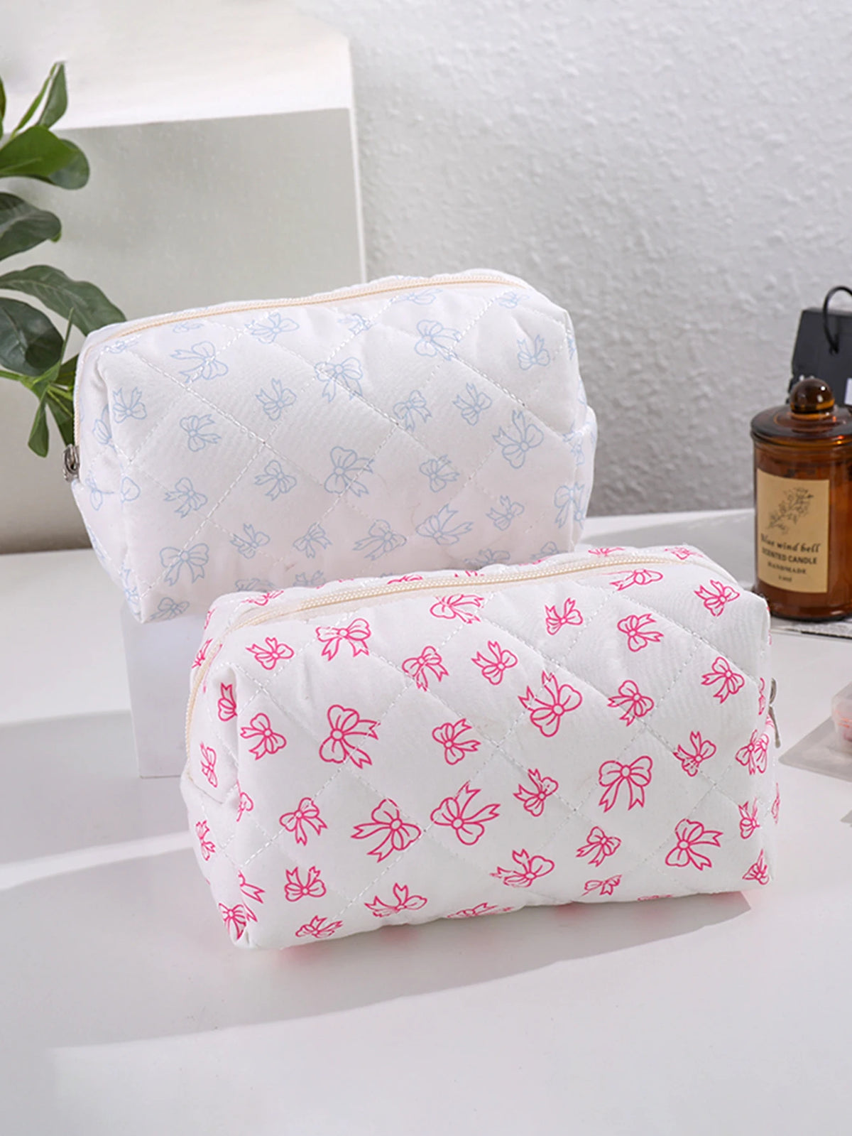 Bolsas de maquillaje acolchadas blancas con estampados de lazo rosa, exhibidas sobre una superficie blanca.