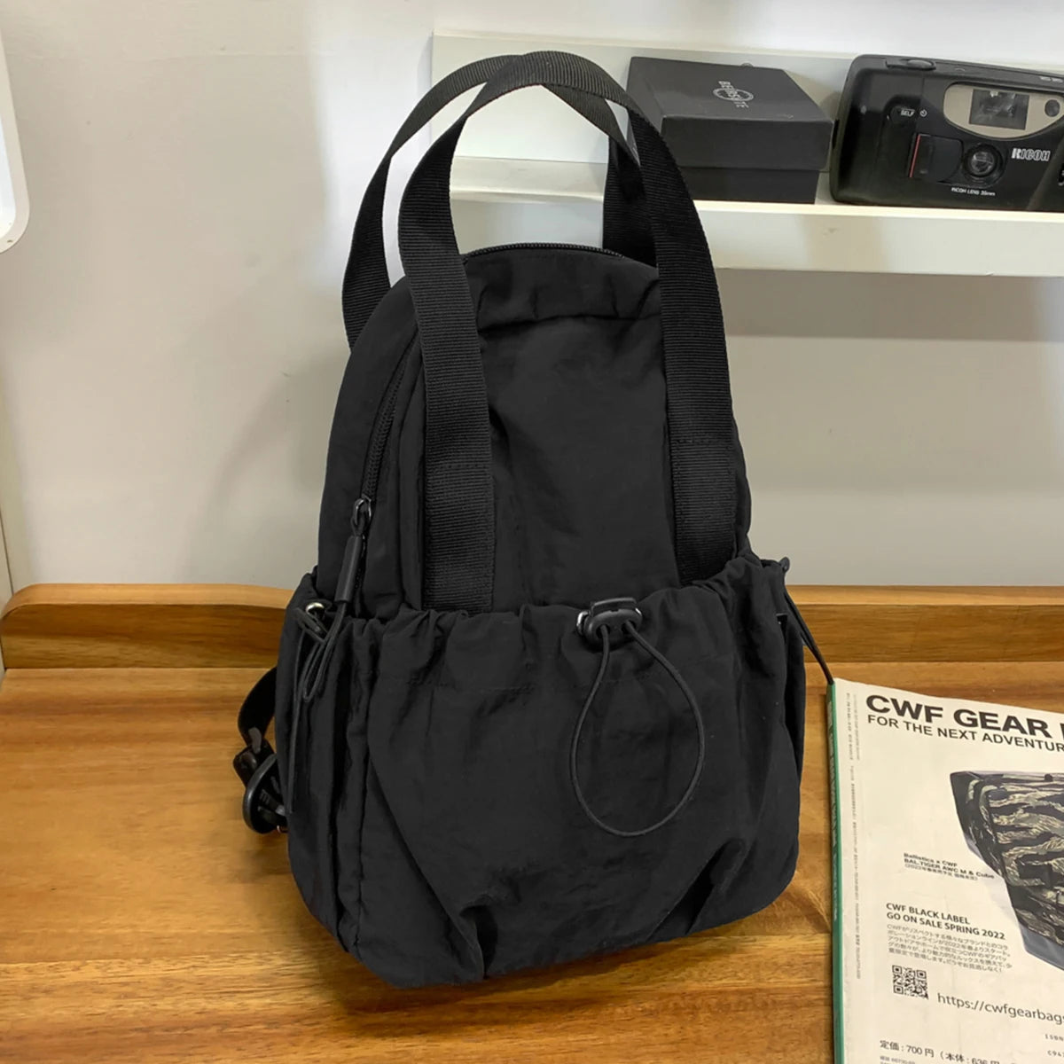 A black versatile casual backpack for women with a laptop compartment resting on a wooden surface.